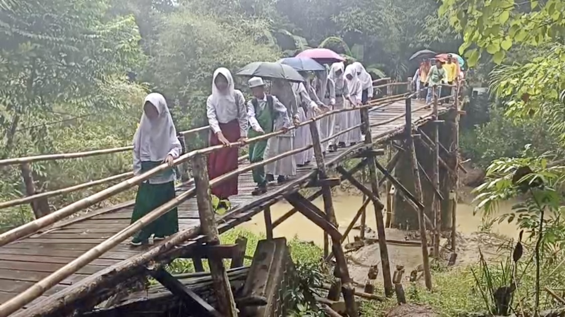 Anak-anak sekolah bersama warga Desa Cikeusik, Kecamatan Cikeusik, Kabupaten Pandeglang, terlihat berhati-hati saat melintasi jembatan Blengbeng yang sudah miring dan rusak parah, beberapa waktu lalu.