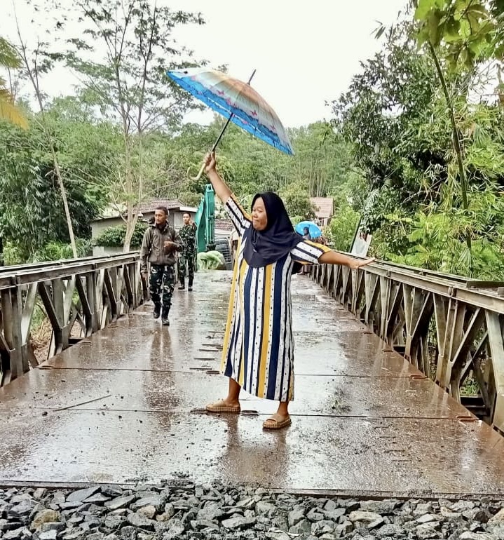 EKSPRESI BAHAGIA. Salah seorang emak-emak warga Desa Kramatjaya, Kecamatan Cimanggu, Kabupaten Pandeglang, sambil membawa payung telah menunjukan ekspresi bahagia di jembatan sementara yang telah selesai dibangun, beberapa waktu lalu.