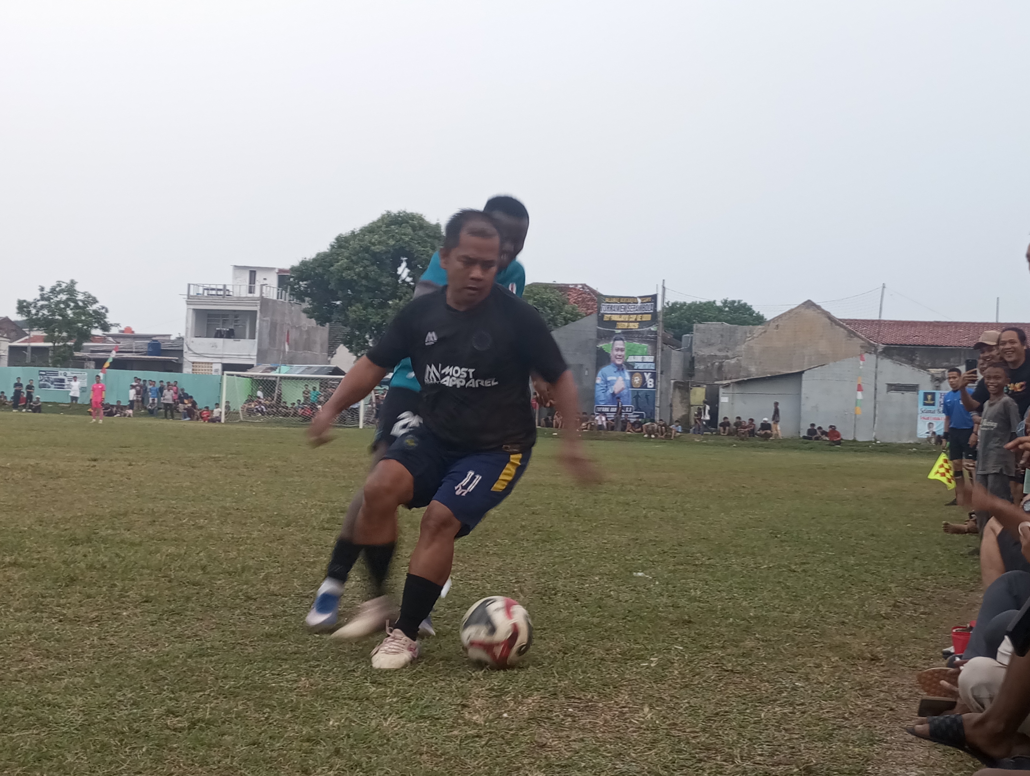 Pemain Tamalo FC, Godel (depan) dikawal pemain asing Cie Allstar pada laga Jumat (26/06/2026). Godel yang diturunkan di pertengahan babak kedua memberikan hiburan segar kepada para penonton lewat aksi-aksinya.(tangselpos.id).