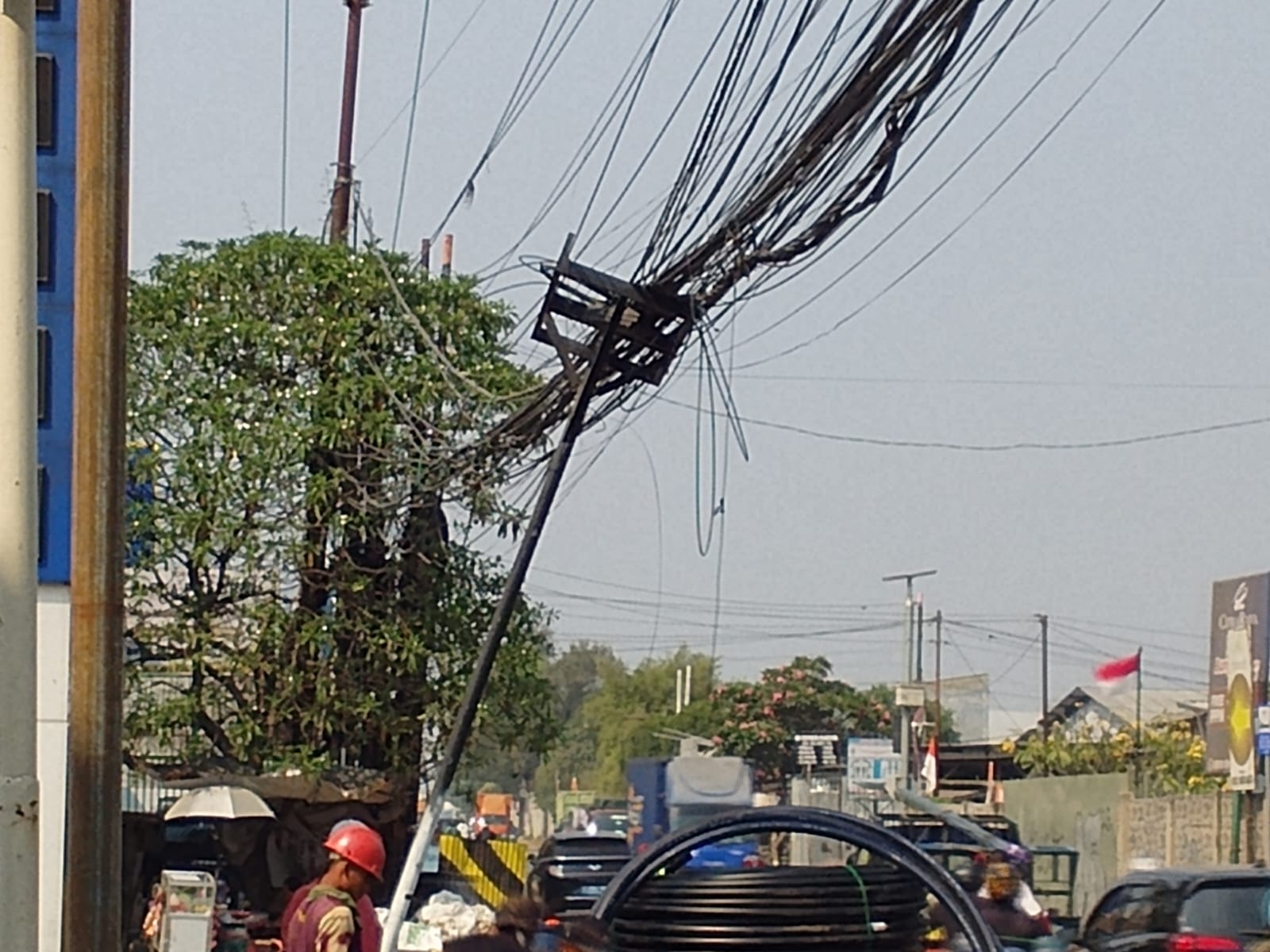 Tiang jaringan kabel yang miring dan membuat sejumlah kabel menjuntai di Jalan Legok, Kabupaten Tangerang. Foto : Gio MG